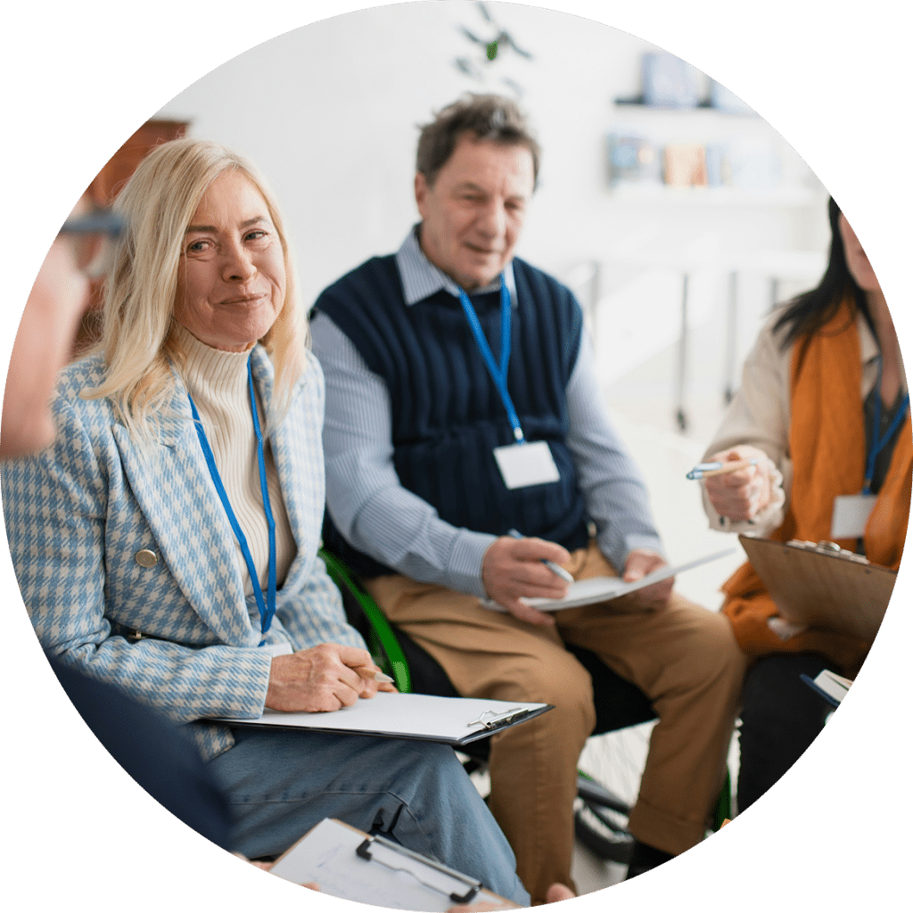A group of people sitting in a circle holding clipboards and participating in a seminar or group meeting.