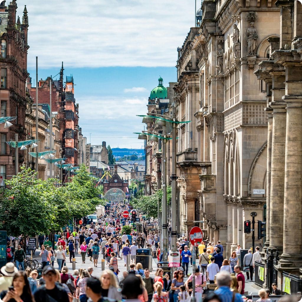 A busy, crowded pedestrian street lined with ornate historic stone buildings.