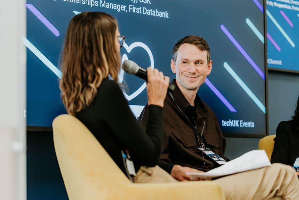 Alasdair Cowie-Fraser, Chief Technology and Product Officer at HDRS, speaking on stage at a techUK event, seated in conversation with a panel
